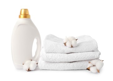 Photo of Bottle of fabric softener, stacked towels and cotton flowers isolated on white