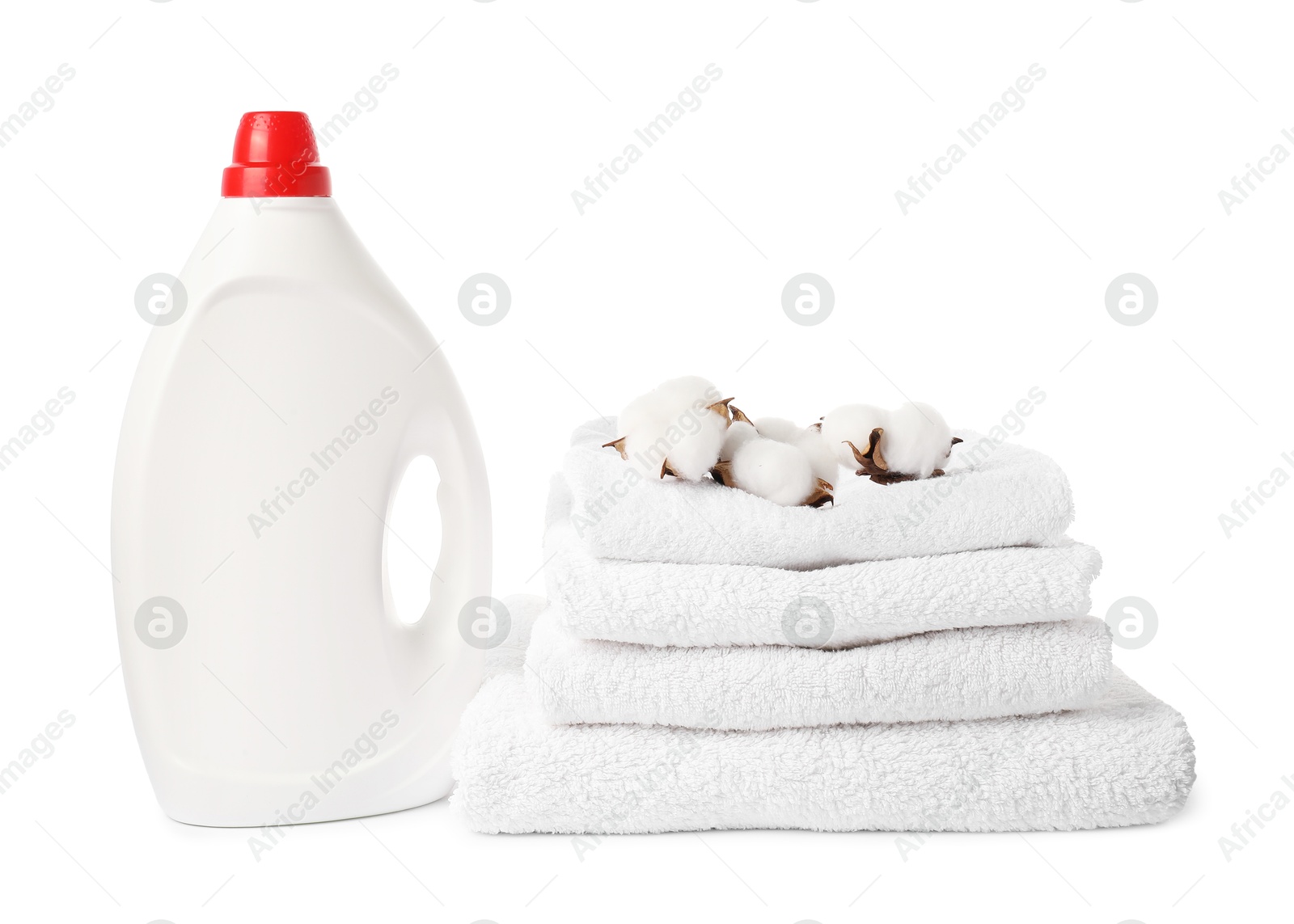 Photo of Bottle of fabric softener, stacked towels and cotton flowers isolated on white