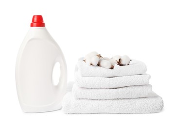 Photo of Bottle of fabric softener, stacked towels and cotton flowers isolated on white