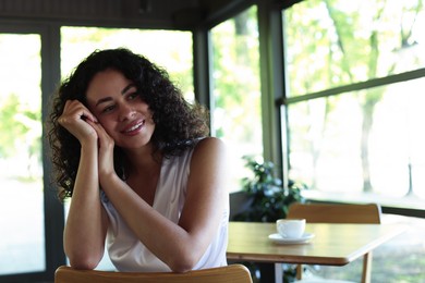 Photo of Portrait of smiling Latin American woman sitting on chair in cafe