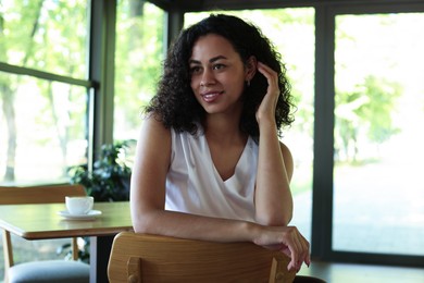 Photo of Portrait of smiling Latin American woman sitting on chair in cafe