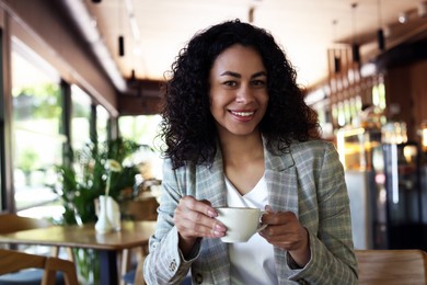 Photo of Portrait of smiling Latin American woman drinking coffee in cafe