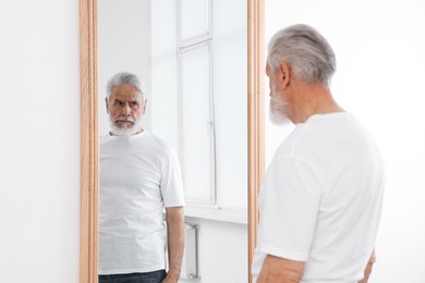 Photo of Handsome senior man looking at himself in mirror indoors
