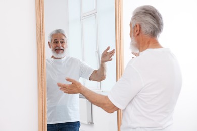 Photo of Handsome senior man looking at himself in mirror indoors