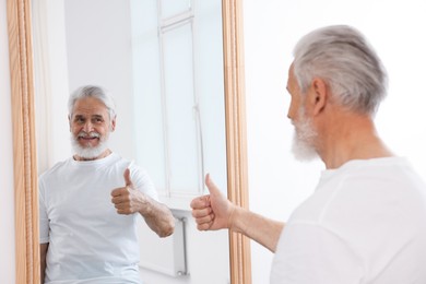 Photo of Handsome senior man showing thumbs up near mirror indoors