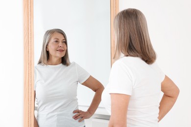 Photo of Beautiful senior woman looking at herself in mirror indoors