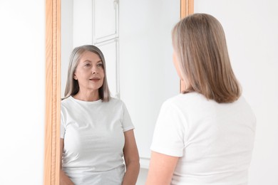 Photo of Beautiful senior woman looking at herself in mirror indoors