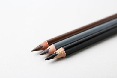 Photo of Three different eyebrow pencils on light background, closeup. Space for text