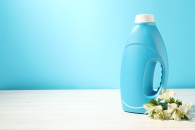Photo of Bottle of fabric softener and lily flowers on white wooden table against light blue background. Space for text