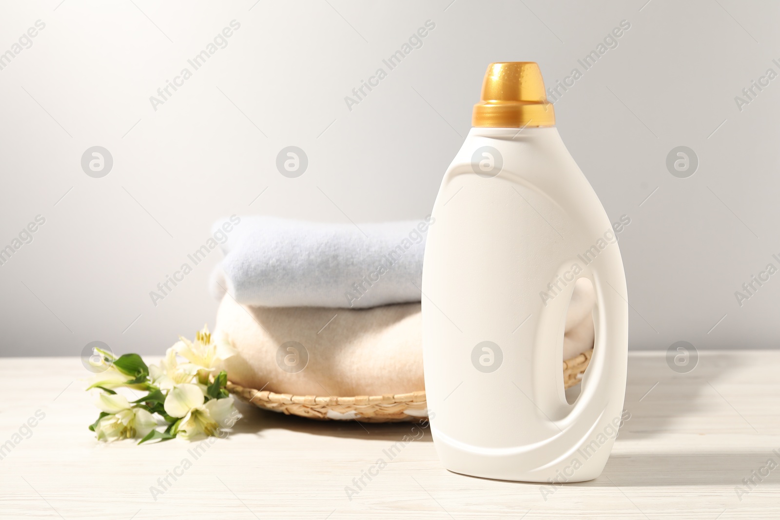 Photo of Bottle of fabric softener, clean clothes and lily flowers on white wooden table