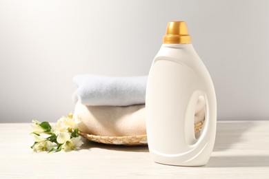 Photo of Bottle of fabric softener, clean clothes and lily flowers on white wooden table