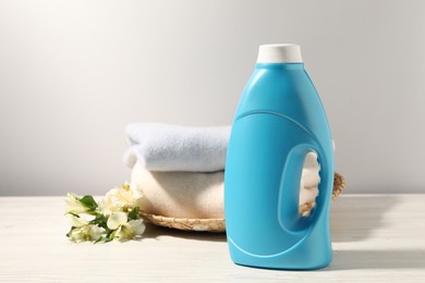 Photo of Bottle of fabric softener, clean clothes and lily flowers on white wooden table