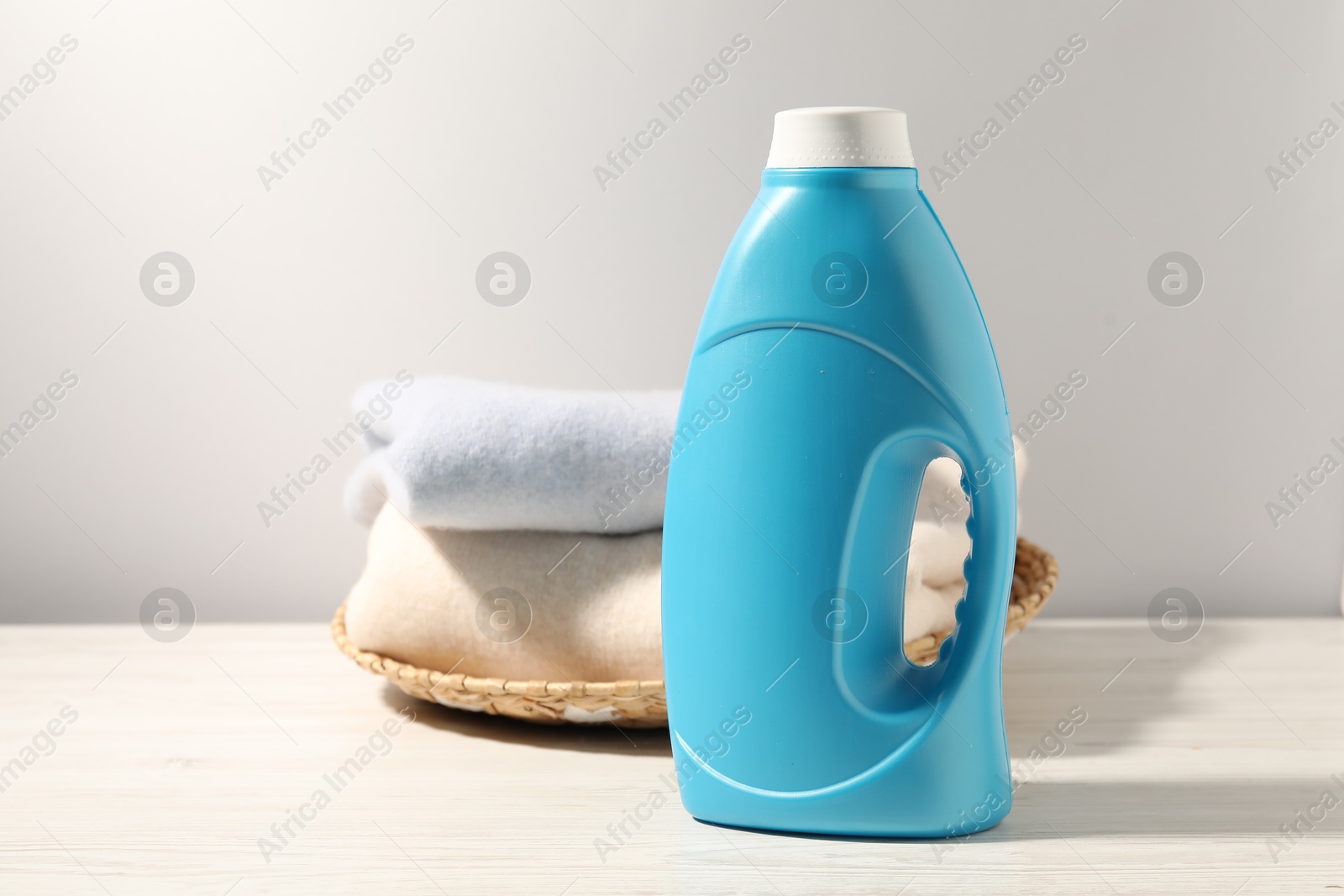 Photo of Bottle of fabric softener and clean clothes on white wooden table