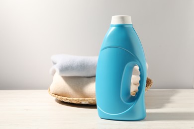 Photo of Bottle of fabric softener and clean clothes on white wooden table