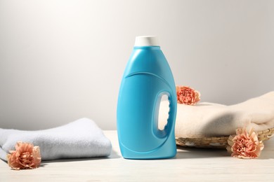 Photo of Bottle of fabric softener, clean clothes and carnation flowers on white wooden table