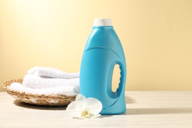 Photo of Bottle of fabric softener, terry towels and orchid flower on white wooden table against light yellow background