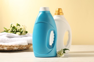 Photo of Bottles of fabric softener, terry towels and lily flowers on white wooden table against light yellow background