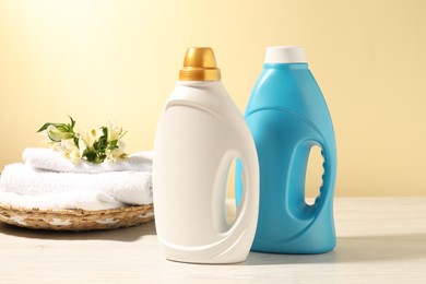 Photo of Bottles of fabric softener, terry towels and lily flowers on white wooden table against light yellow background