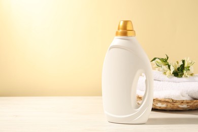 Photo of Bottle of fabric softener, terry towels and lily flowers on white wooden table against light yellow background. Space for text