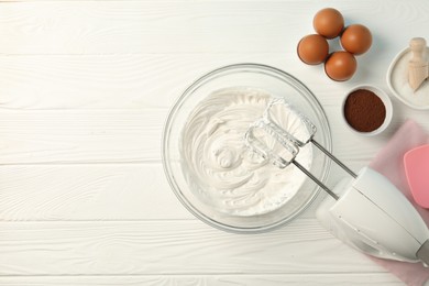 Photo of Bowl with whipped cream, hand mixer and ingredients on white wooden table, flat lay. Space for text