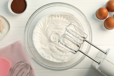 Photo of Bowl with whipped cream, hand mixer and ingredients on white wooden table, flat lay