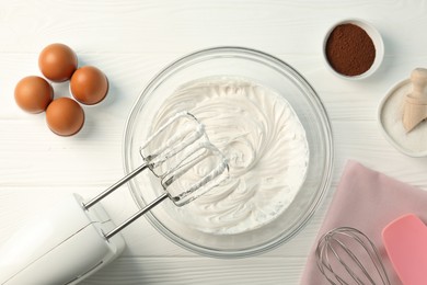 Photo of Bowl with whipped cream, hand mixer and ingredients on white wooden table, flat lay