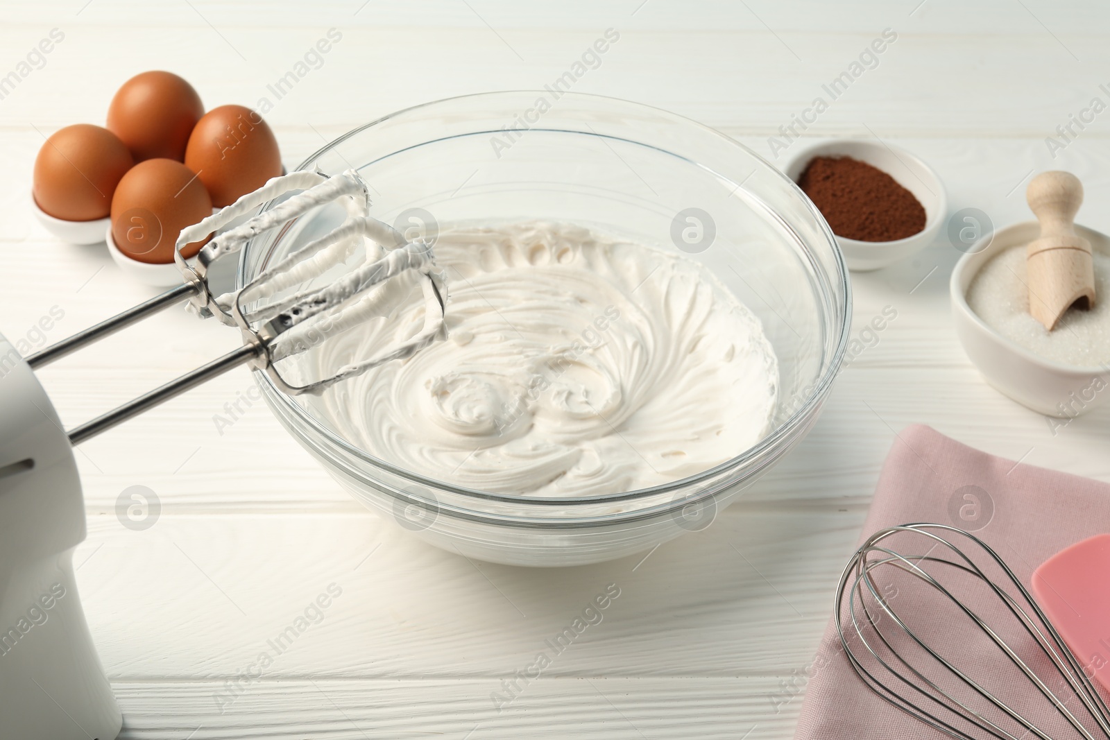 Bowl with whipped cream, hand mixer, whisk and ingredients on white wooden table, closeup Photo of Bowl with whipped cream, hand mixer, whisk and ingredients on white wooden table, closeup