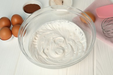 Photo of Bowl with whipped cream, whisk and ingredients on white wooden table, closeup