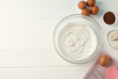 Photo of Bowl with whipped cream, whisk and ingredients on white wooden table, flat lay. Space for text
