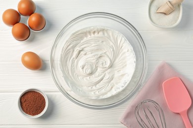 Photo of Bowl with whipped cream, whisk and ingredients on white wooden table, flat lay