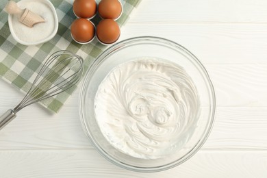Photo of Bowl with whipped cream, whisk and ingredients on white wooden table, flat lay