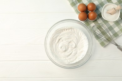 Photo of Bowl with whipped cream, whisk and ingredients on white wooden table, flat lay. Space for text