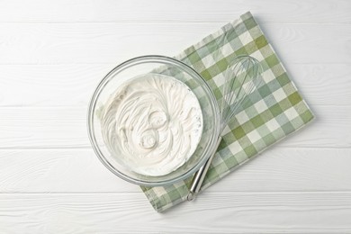 Photo of Bowl with whipped cream and whisk on white wooden table, top view