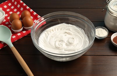 Photo of Bowl with whipped cream and ingredients on wooden table, closeup