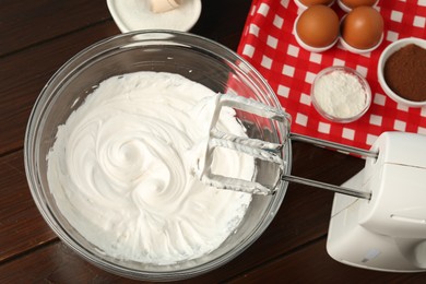 Photo of Bowl with whipped cream, hand mixer and ingredients on wooden table, flat lay