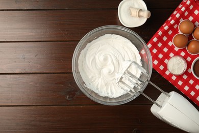Photo of Bowl with whipped cream, hand mixer and ingredients on wooden table, flat lay. Space for text
