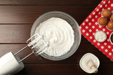 Photo of Bowl with whipped cream, hand mixer and ingredients on wooden table, flat lay