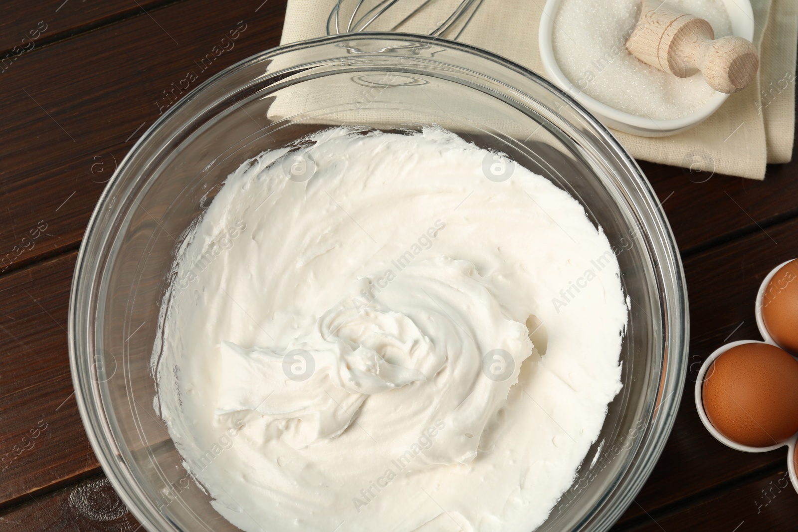 Bowl with whipped cream, whisk and ingredients on wooden table, flat lay Photo of Bowl with whipped cream, whisk and ingredients on wooden table, flat lay