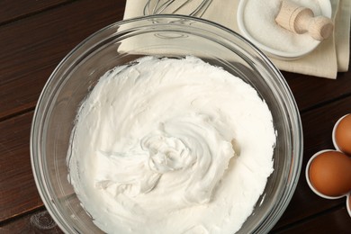Photo of Bowl with whipped cream, whisk and ingredients on wooden table, flat lay
