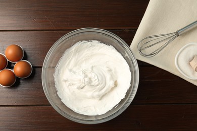 Photo of Bowl with whipped cream, whisk and ingredients on wooden table, flat lay