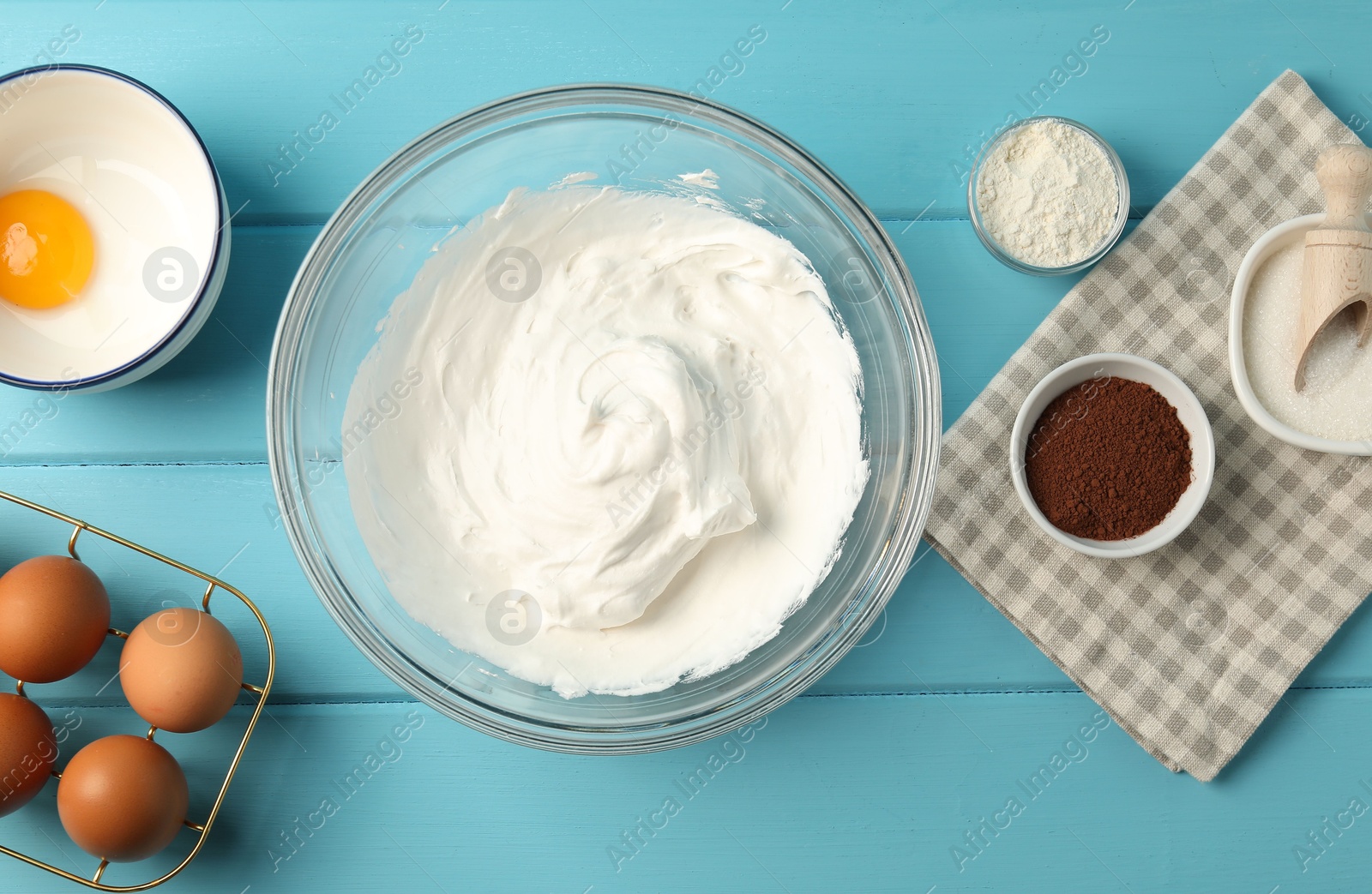 Bowl with whipped cream and ingredients on light blue wooden table, flat lay Photo of Bowl with whipped cream and ingredients on light blue wooden table, flat lay