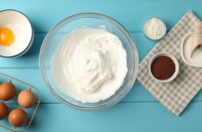 Photo of Bowl with whipped cream and ingredients on light blue wooden table, flat lay