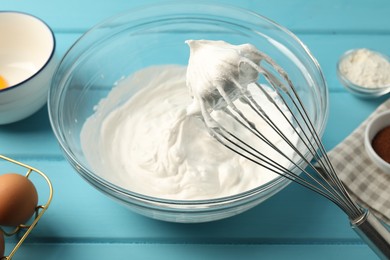 Photo of Bowl with whipped cream, whisk and ingredients on light blue wooden table, closeup