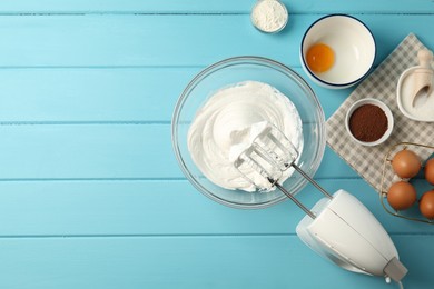 Photo of Bowl with whipped cream, hand mixer and ingredients on light blue wooden table, flat lay