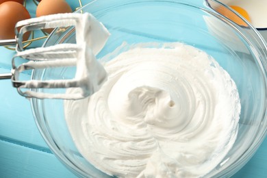 Photo of Bowl with whipped cream, hand mixer and ingredients on light blue wooden table, closeup