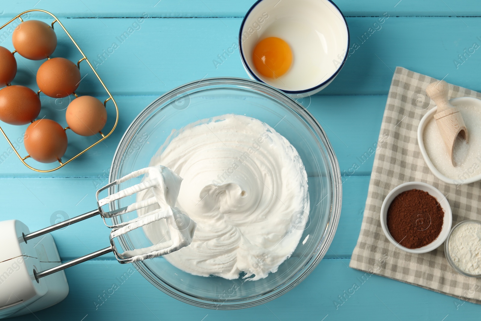 Bowl with whipped cream, hand mixer and ingredients on light blue wooden table, flat lay Photo of Bowl with whipped cream, hand mixer and ingredients on light blue wooden table, flat lay