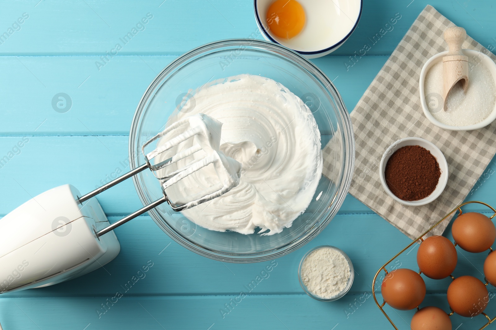 Bowl with whipped cream, hand mixer and ingredients on light blue wooden table, flat lay Photo of Bowl with whipped cream, hand mixer and ingredients on light blue wooden table, flat lay