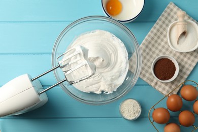Photo of Bowl with whipped cream, hand mixer and ingredients on light blue wooden table, flat lay