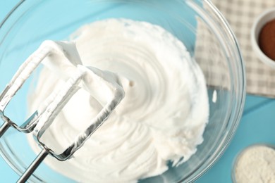 Photo of Bowl with whipped cream, hand mixer and ingredients on light blue wooden table, flat lay