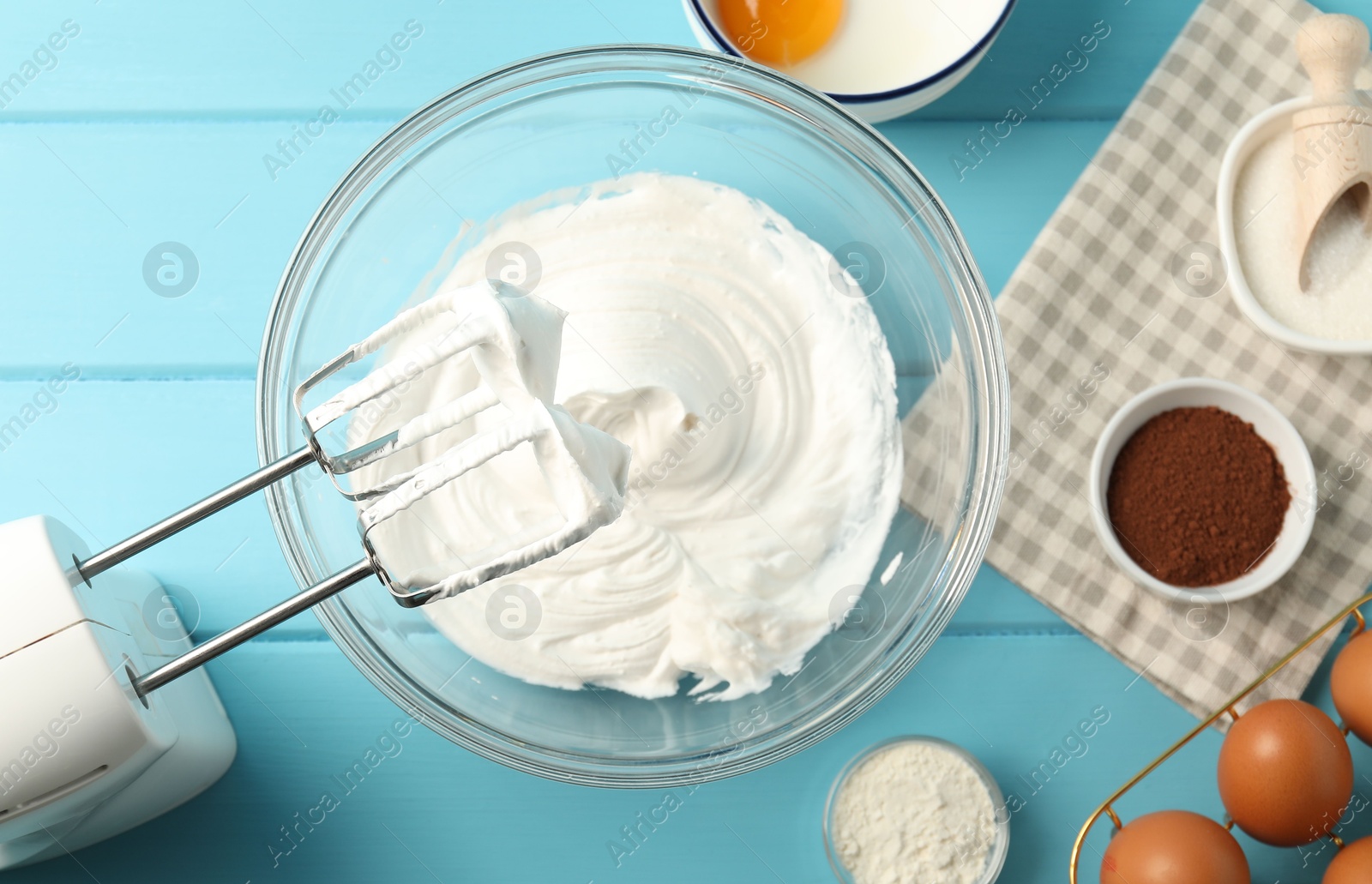 Bowl with whipped cream, hand mixer and ingredients on light blue wooden table, flat lay Photo of Bowl with whipped cream, hand mixer and ingredients on light blue wooden table, flat lay